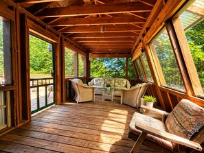 Une véranda couverte avec des poutres en bois, de grandes fenêtres et du mobilier d’extérieur.