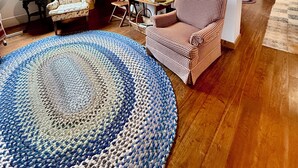 A cozy room with a wooden ceiling, a round blue and white rug, a checkered sofa, a chair, and a staircase leading to another room. - Rustic Pine Lodge - Cozy 4 BR Adirondack Escape (Schroon Lake)