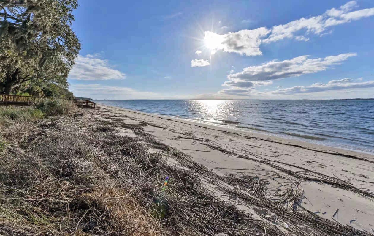 A beach with a wooden fence, clear sky, and calm water.