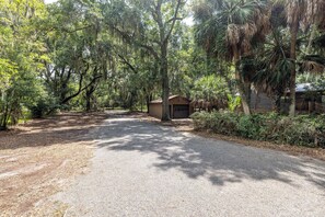 A gravel driveway leading to a wooden cabin with a garage, surrounded by dense trees and greenery.