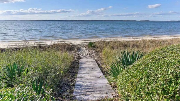 Un sendero que lleva a una playa, con vista despejada al agua y a la costa distante.