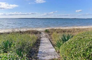 Un sendero que lleva a una playa, con vista despejada al agua y a la costa distante.