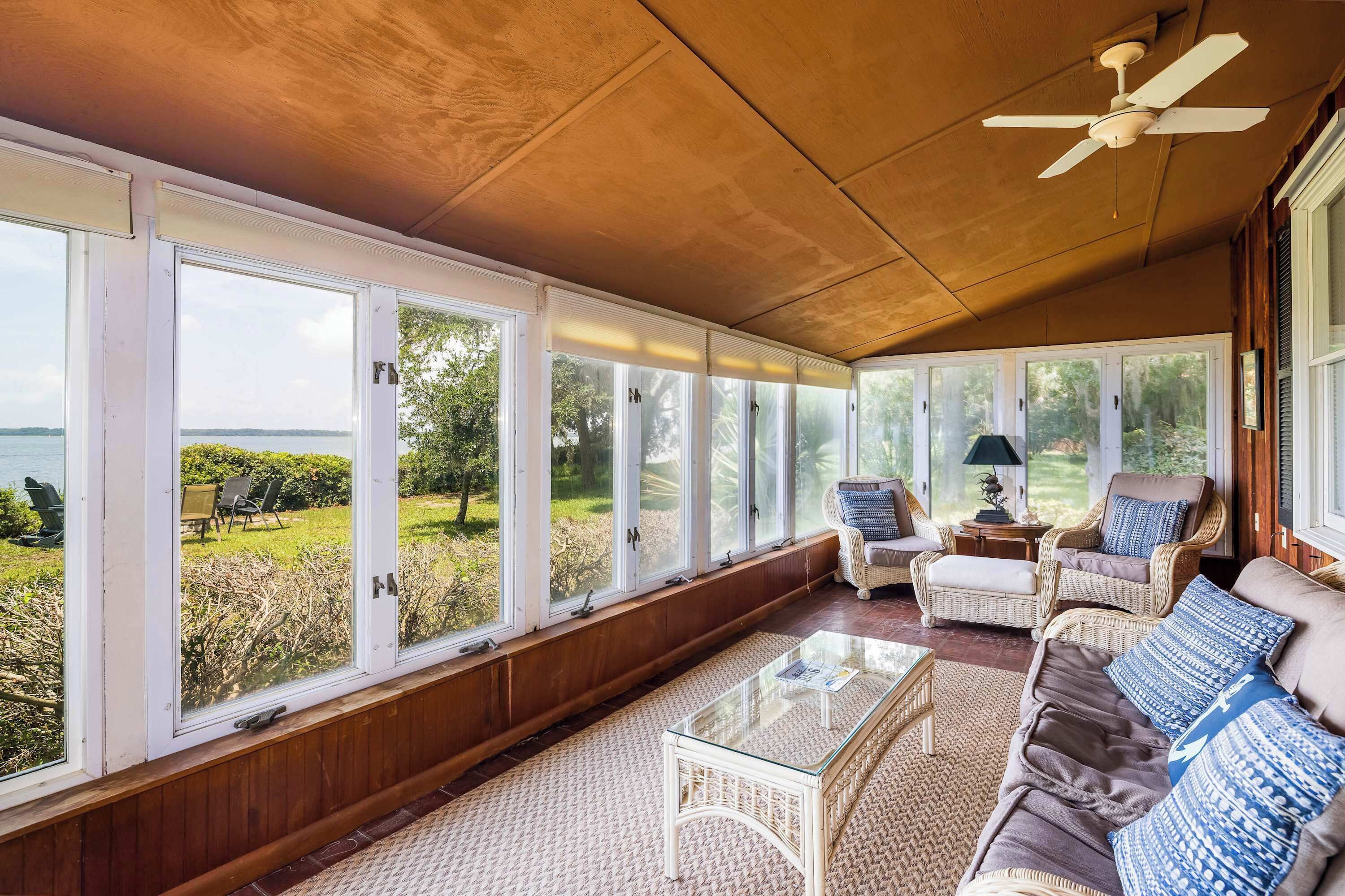 Une véranda avec de grandes fenêtres, des meubles en osier et un ventilateur de plafond.