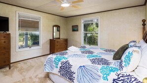 Un dormitorio con cama, cómoda, ventilador de techo y ventanas.
