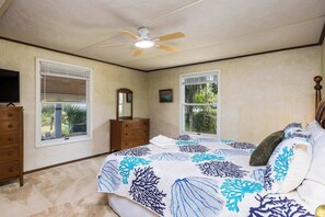 A bedroom with a bed, dresser, ceiling fan, and windows.