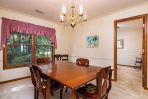 A dining room with a wooden table and chairs, a chandelier, a window with a view of trees, and a painting on the wall.