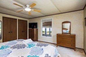 A bedroom with a bed, a dresser, a mirror, a ceiling fan, and a window with blinds.
