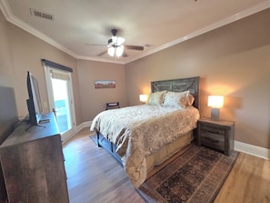 A bedroom with a bed, bedside lamps, a ceiling fan, a desk with a computer, and a window.