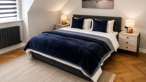 Een slaapkamer met een bed, twee nachtkastjes, een radiator, een raam met zonwering, en een schilderij aan de muur.
