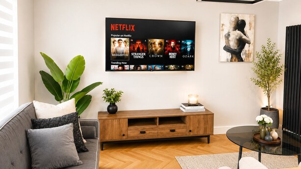 Een moderne woonkamer met een flatscreen televisie waarop een Netflix-interface wordt getoond, een bank, een salontafel en een potplant.
