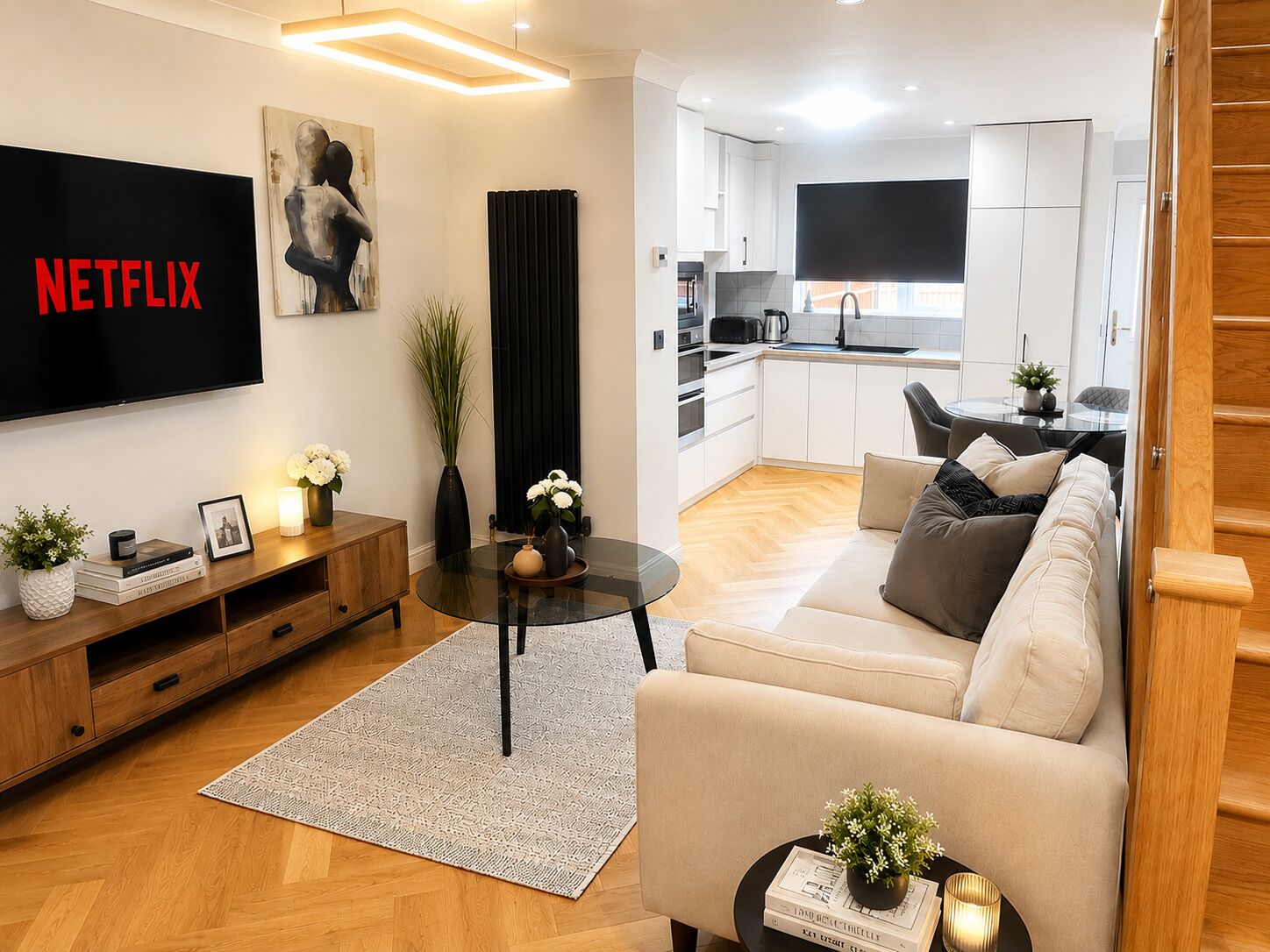 A modern living room with a flat-screen TV, a sofa, a coffee table, and a kitchen in the background.