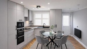 Een moderne keuken met grijze kastjes, een zwarte magnetron en een ronde glazen tafel met grijze stoelen.