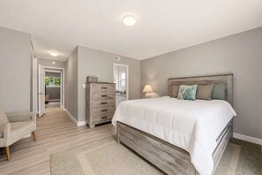 A bedroom with a bed, dresser, chair, and a hallway leading to another room. - 5BR Hot Tub Retreat | Sleeps 14 & BBQ (Spring Valley)