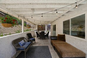 A covered outdoor seating area with wicker furniture, a table, and chairs, and a large window on one side.