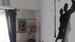 Een kamer met een bureau, planken, een telefoon, een lamp en een decoratie aan de muur.