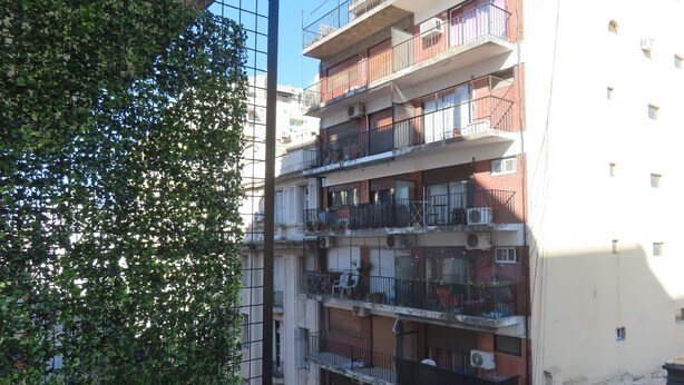 Een meerlaags woongebouw met balkons, airconditioning en een zichtbare boom.
