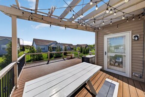 A covered outdoor deck with a table and chairs, a pergola with string lights, and a view of neighboring houses.