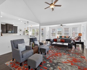 Un salon spacieux avec un canapé gris, un pouf et un tapis à motifs.