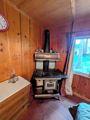 A rustic wooden room with a vintage stove, a wooden dresser, and a window with a view of trees. - Sequoia Time Capsule: Spa, Walk 2 Giant Sequoias, River, Fish, Bike, Saloon (Springville)