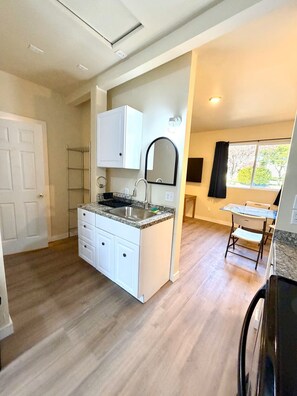 A kitchen with a granite countertop, white cabinetry, a stainless steel sink, and a window with a view of trees. - Brown Door at Lake Serene (Lynnwood)