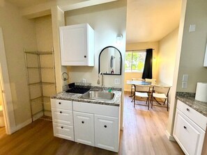 A compact kitchen with a granite countertop, white cabinetry, and a dining area with a table and chairs. - Brown Door at Lake Serene (Lynnwood)