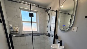A modern bathroom with a glass-enclosed shower, a toilet, a sink, and a mirror.
