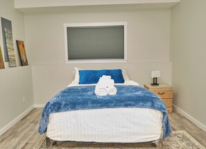 Ein Schlafzimmer mit Bett, Kissen, Nachttisch, Lampe und Bildern an der Wand.