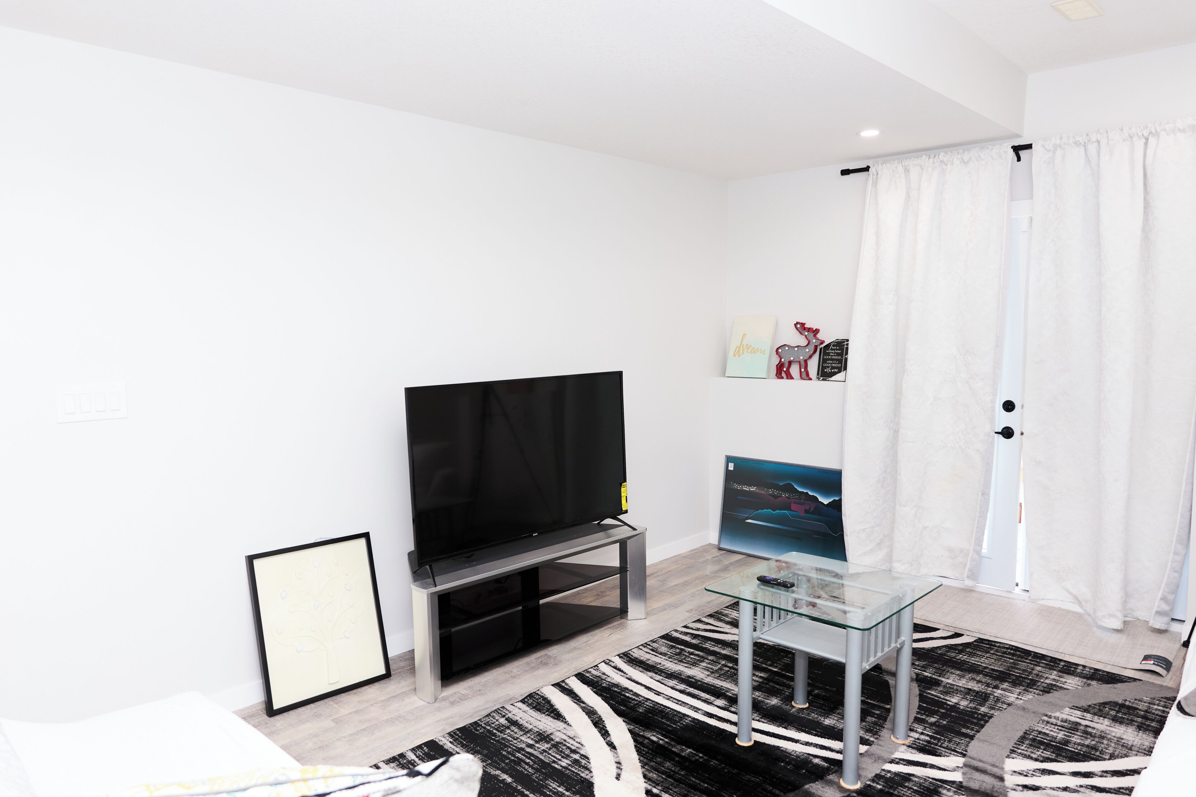 A modern living room with a flat-screen TV, a glass coffee table, and a black-and-white patterned rug.