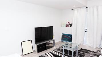A modern living room with a flat-screen TV, a glass coffee table, and a black-and-white patterned rug.