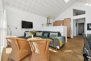 Ein modernes Wohnzimmer mit einer Couch, Korbstühlen, einem Flachbildfernseher und einer Küchenzeile im Hintergrund.