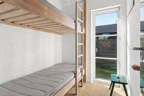Ein Stockbett mit einer Leiter, ein kleiner Hocker und eine Schiebetür zu einem Außenbereich.