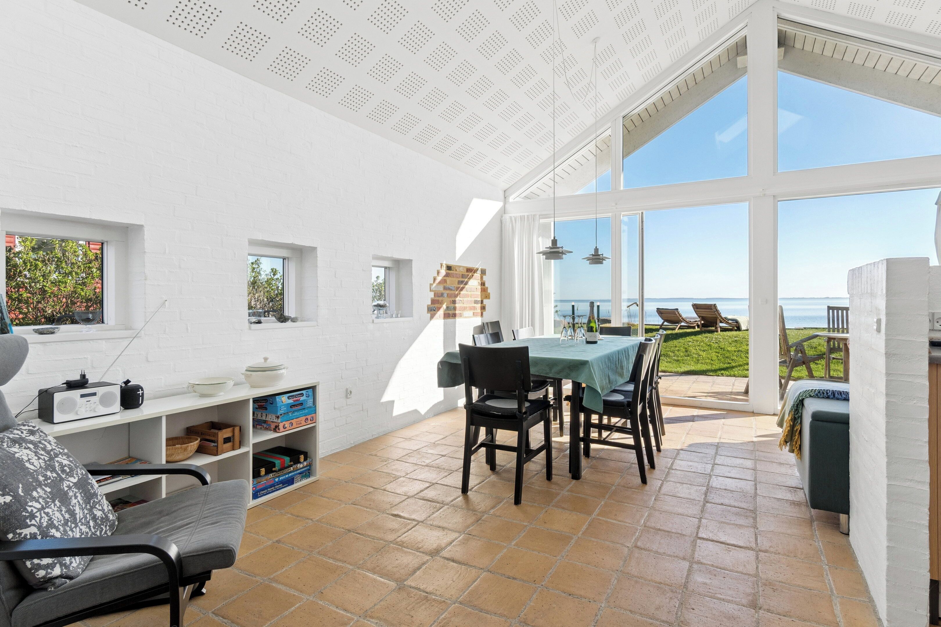 Ein heller, offener Wohnbereich mit Terrasse und Meerblick, ausgestattet mit Esstisch, Stühlen und einer Couch.
