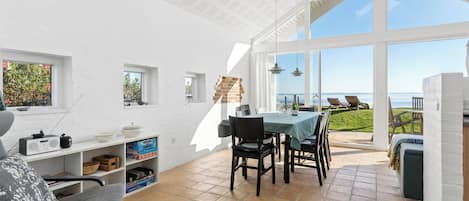 Ein heller, offener Wohnbereich mit Terrasse und Meerblick, ausgestattet mit Esstisch, Stühlen und einer Couch.