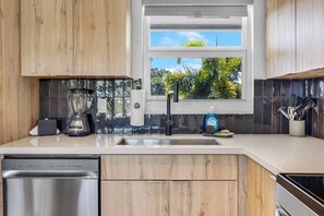 Una cucina moderna con mobili in legno, una lavastoviglie in acciaio inossidabile, una finestra vista verde e uno schienale piastrellato.