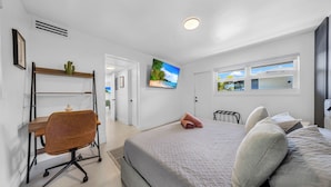 Une chambre à coucher avec un lit, un bureau et une chaise, un téléviseur fixé au mur et une fenêtre.