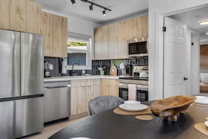 A modern kitchen with stainless steel appliances, wooden cabinets, and a dining area with a dark table and chairs. - Boutique Stay - Resort -5min to beach-near shop (Fort Lauderdale)