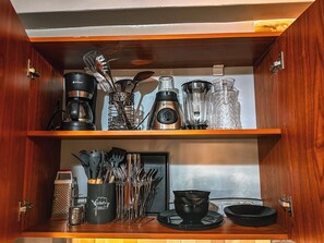 Ein Küchenschrank mit Kaffeemaschine, Mixer und Geschirr.