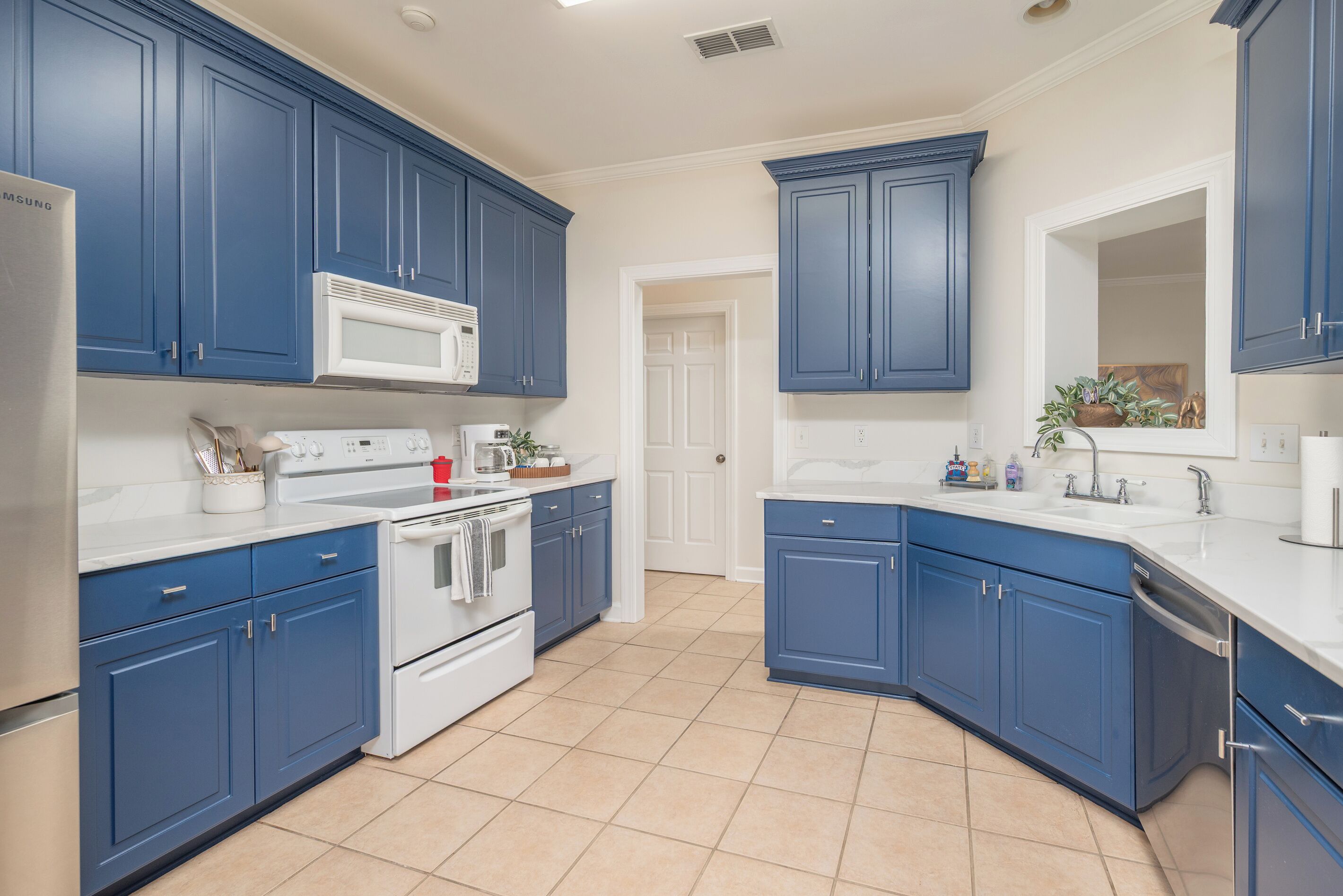 A kitchen with blue cabinets, white appliances, and a tiled floor.