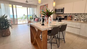 Una cucina moderna con isola centrale, sedie da pranzo, ventilatore a soffitto e vista sull'oceano.