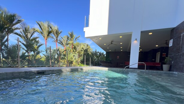 Una piscina con area relax, palme e un edificio moderno.