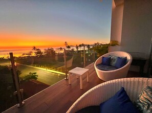 A balcony with a view of the sunset over the ocean, a wicker chair with cushions, and a small table. - Oceanfront Corner Unit  Full Ocean View  Beachfront Pool Parking  Jaco (Jaco)