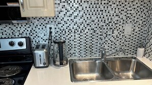 Una cocina con un lavamanos doble, una estufa, un tostador y un cajón con utensilios.