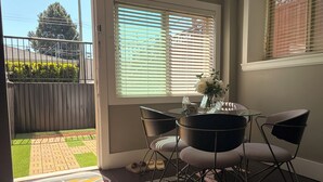 Una habitación con un ventanal de vidrio que da a un balcón, una mesa redonda con sillas y un pequeño florero con flores.
