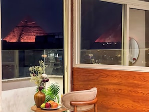 A room with a view of a pyramid at night, a vase with flowers, a fruit plate, and a chair. - Pyramids Palace View (Giza)