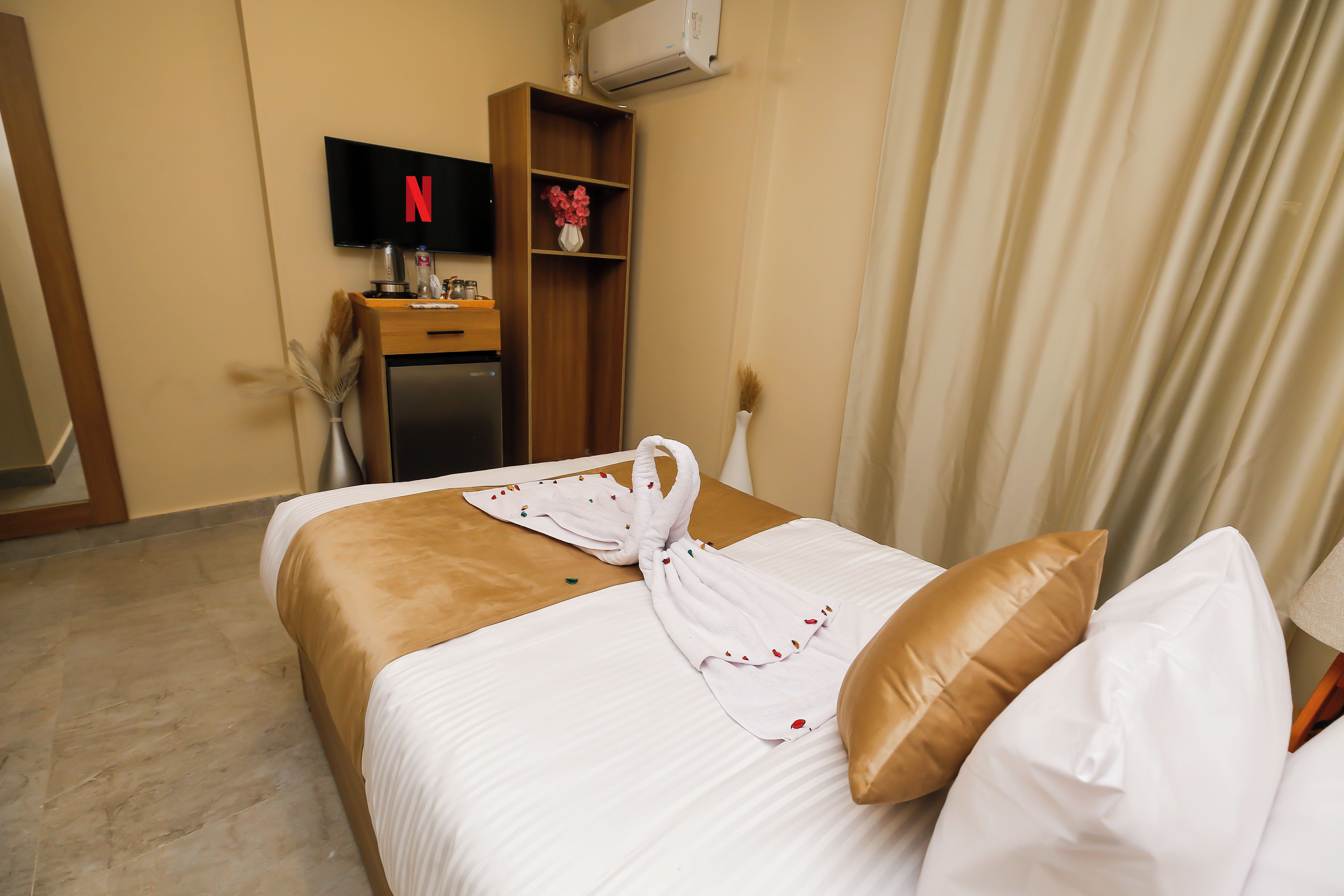 Habitación de hotel con cama, televisor montado en la pared, minibar y ventana con cortinas.