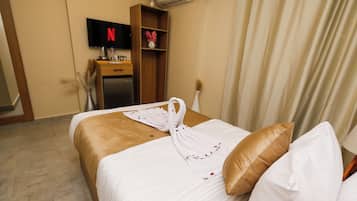 Habitación de hotel con cama, televisor montado en la pared, minibar y ventana con cortinas.