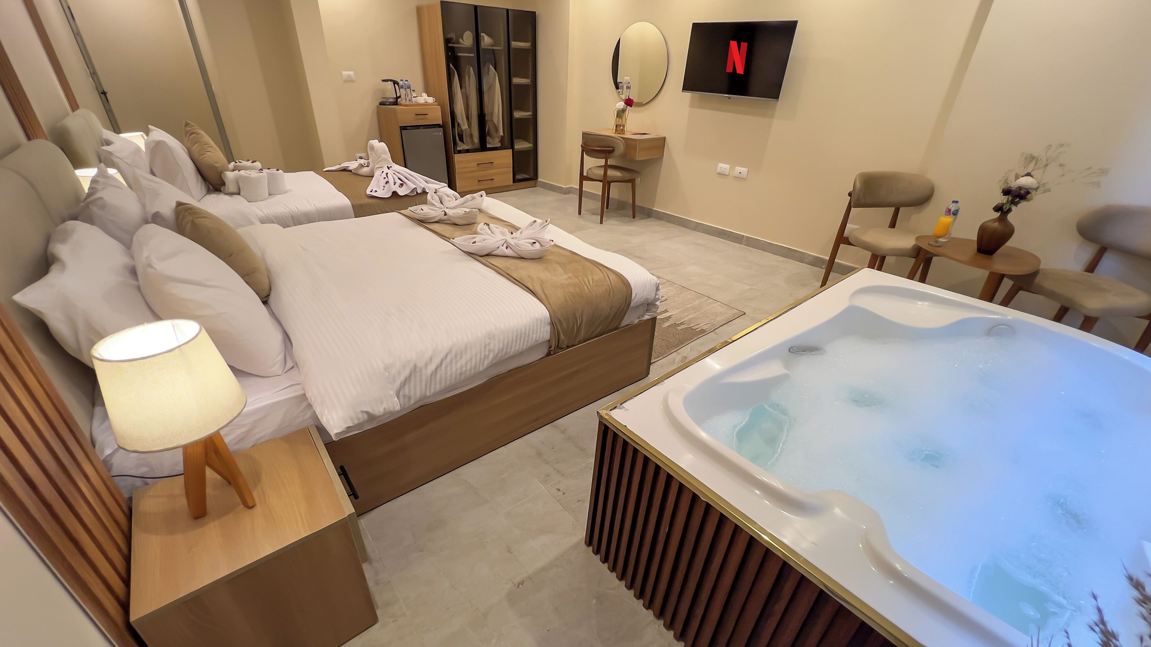A hotel room with a large bed, a sitting area with a table and chairs, a TV mounted on the wall, and a hot tub.
