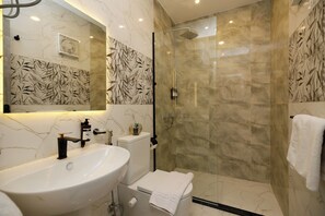 Ein Badezimmer mit einem weißen Waschbecken, einer Toilette, einer Duschkabine mit Glastür und einem Spiegel über dem Waschbecken.