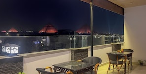 A balcony with a glass table and chairs, overlooking a cityscape with illuminated buildings. - Pyramids Palace View (Giza)