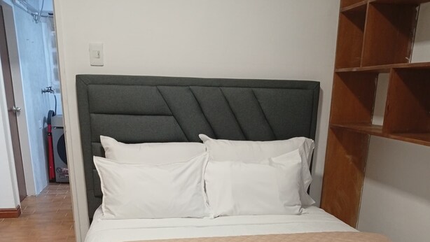 Ein Bett mit gestepptem Kopfteil, weißer Bettwäsche und einem zusammengerollten Handtuch.